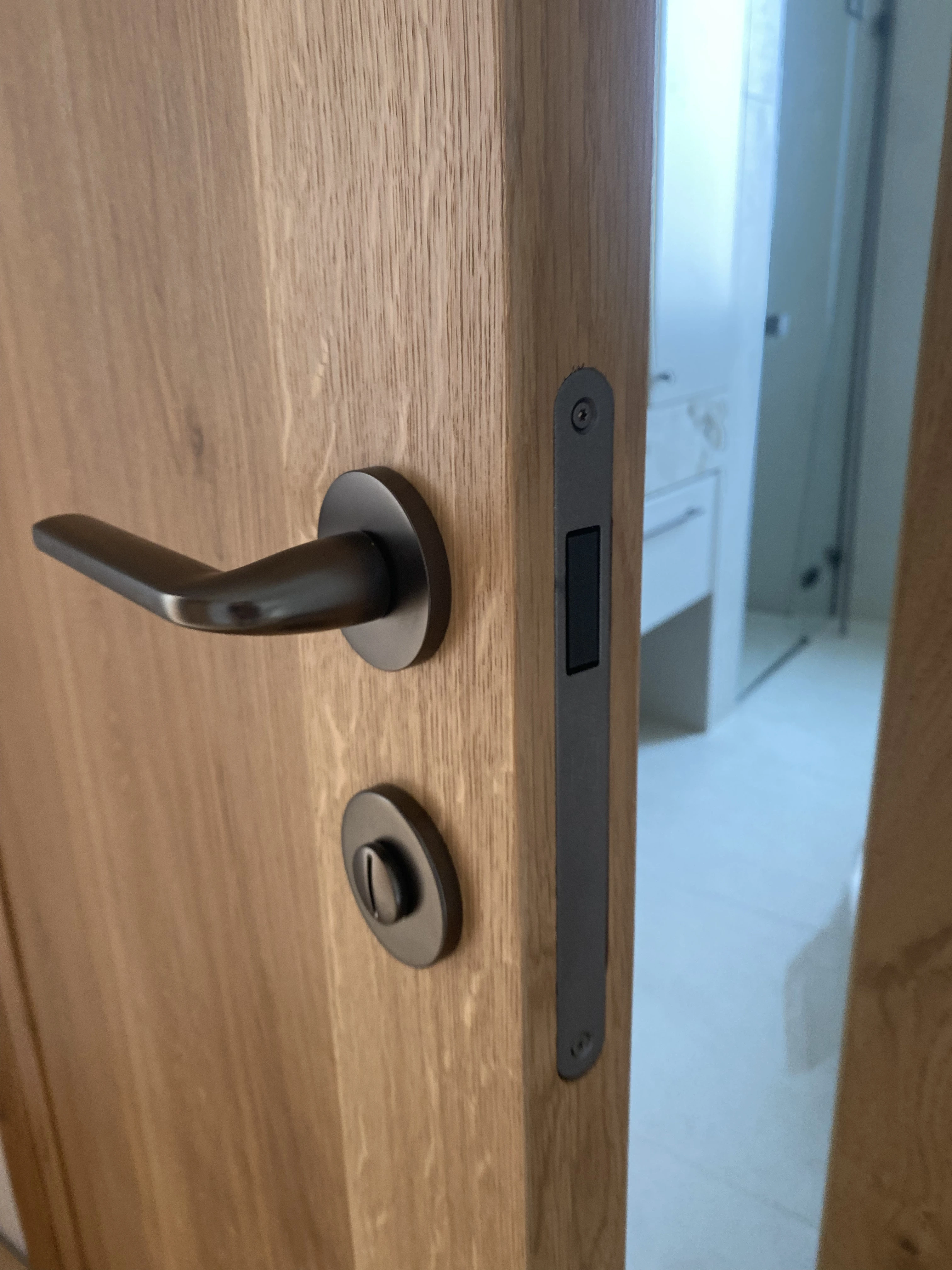 Detal okucia klamka i zamek kolor gunmetal w dębowych drzwiach łazienkowych - realizacja Gliwice